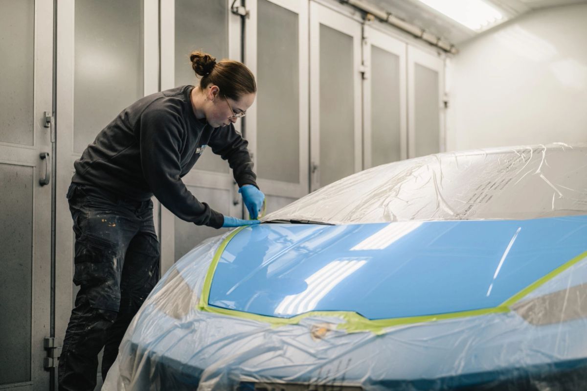 Lackierer klebt ein hellblaues Auto in der Lackierkabine ab